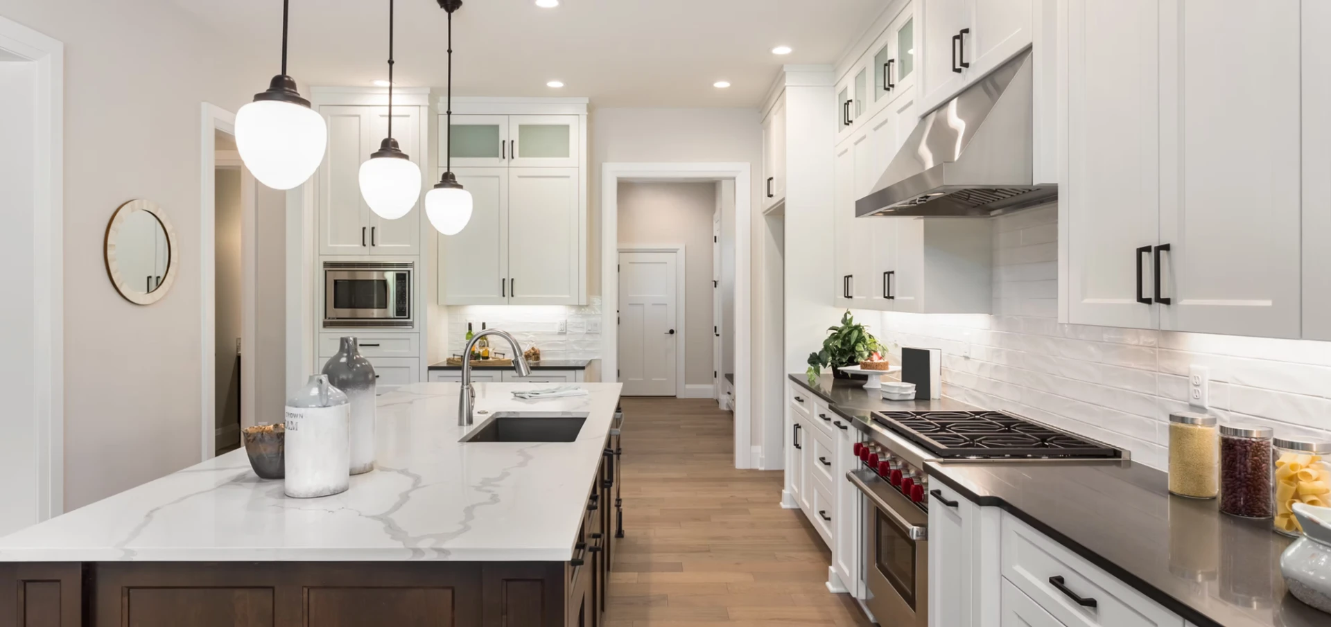Bright white kitchen with a marble island, globe pendant lights, stainless range hood, and subway tile backsplash